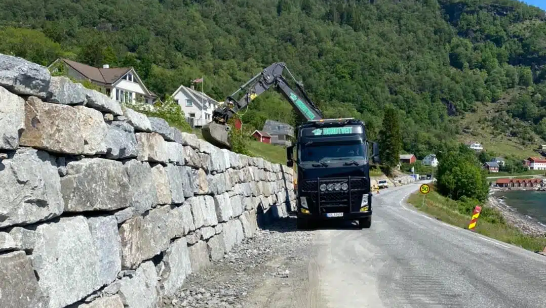 Kranbil som løfter opp stein til steinmur