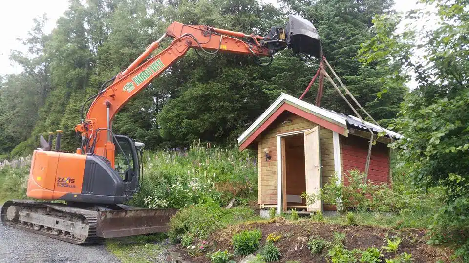Gravemaskin som løfter på plass uthus